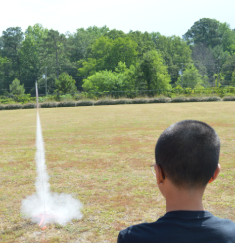Boy watching a rocket engine thrust test in a field.