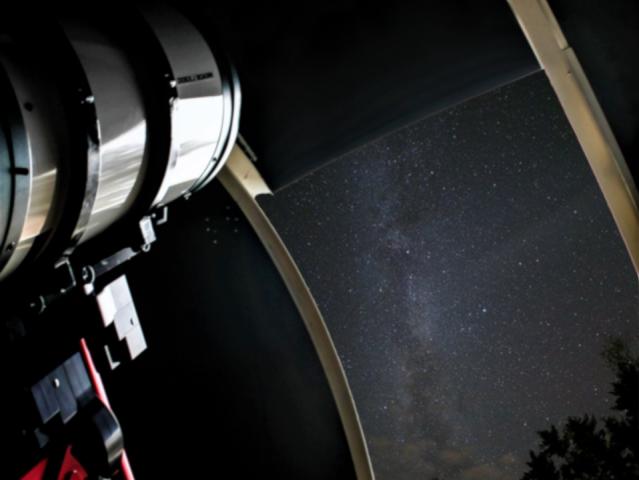 A view of a telescope looking out an observatory opening