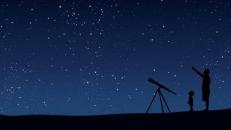 A person with a telescope silhoutted against the night sky.